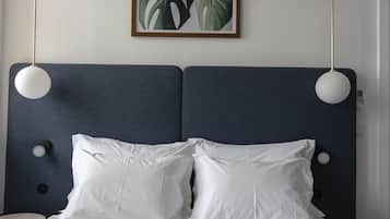 Un lit avec du linge de lit blanc, une tête de lit bleu foncé, deux lampes de chevet et une plante encadrée accrochée au mur.