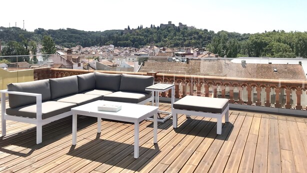 A rooftop terrace with a white sofa set, a small table, and a white bench. The terrace overlooks a cityscape with buildings and a hill with trees. - O Paço - Exclusive Accommodation (Tomar)