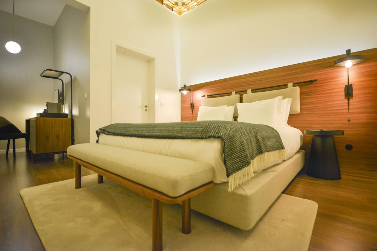 Un dormitorio moderno con cama, banco, mesita de noche y cabecero de madera.