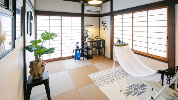 A traditional Japanese room with tatami flooring, a hammock, a desk with a chair, and a large window with shoji screens. - Wave House 99 (Kujukuri)
