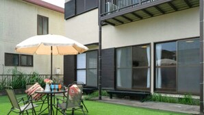 An outdoor patio with a table and chairs, a white umbrella, and a small garden area. - Wave House 99 (Kujukuri)