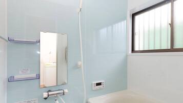 A bathroom with a bathtub, a shower, a mirror, and a window.