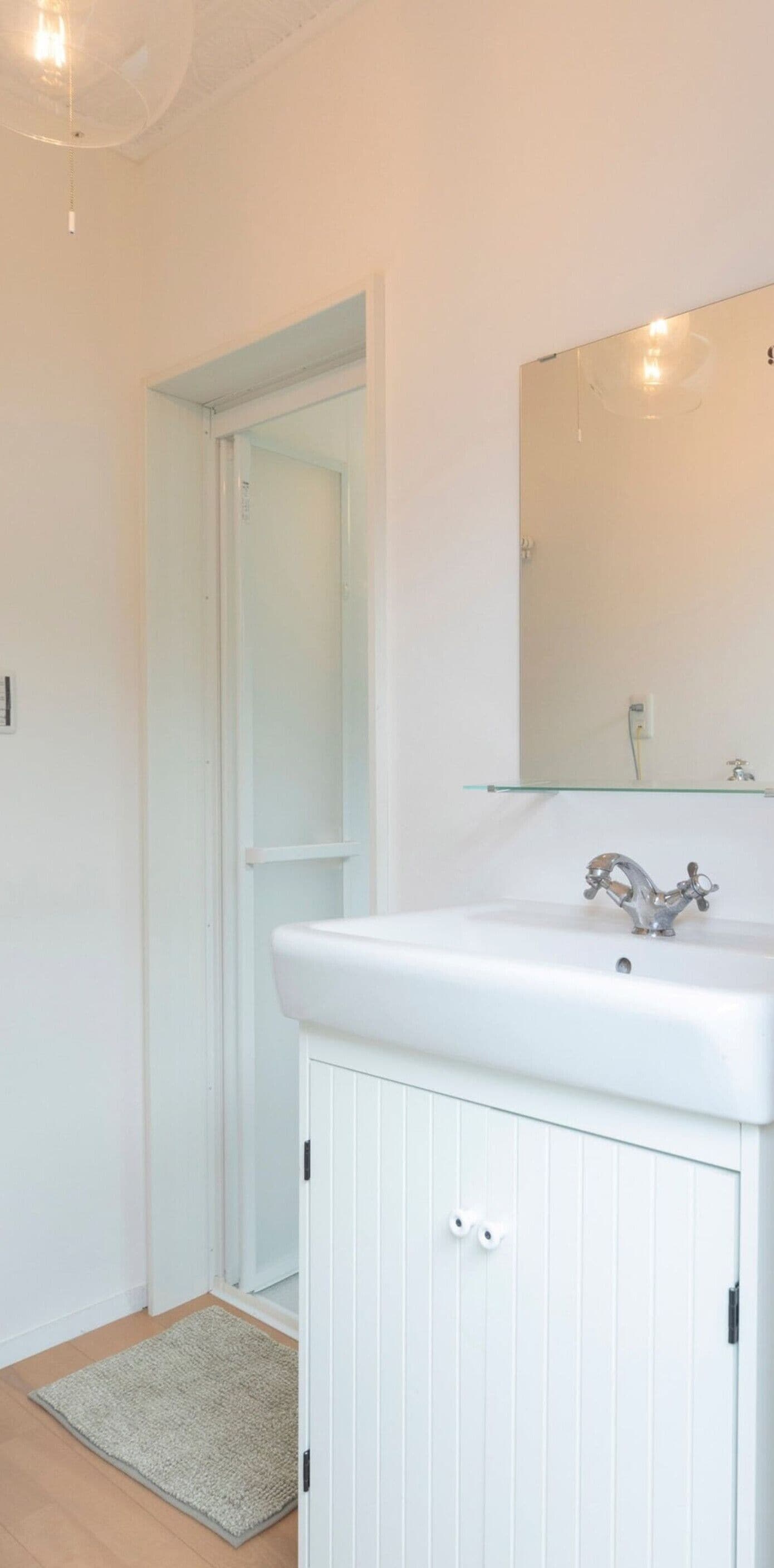 A bathroom with a white sink, mirror, and door leading to another room.