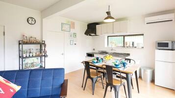 Een kleine keuken met witte kastjes, een eettafel met stoelen, een blauwe bank en een klok aan de muur.