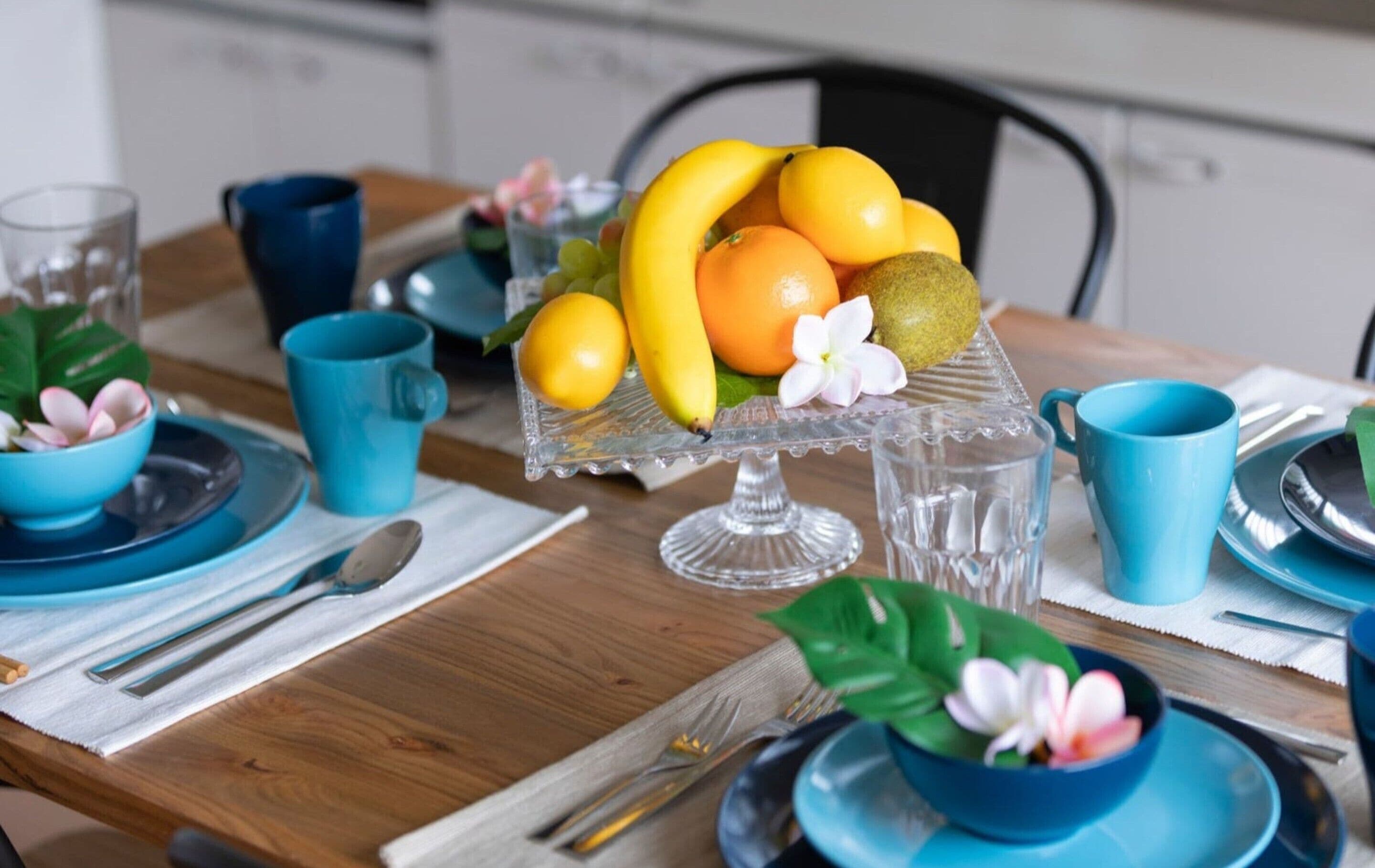 Une table à manger dressée avec de la vaisselle bleue, un centre de table composé de fruits et une tasse bleue.