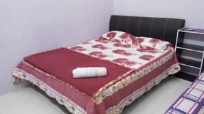 A small, neatly made bed with a floral bedspread and a red blanket, a black headboard, and a small shelf unit beside the bed. - Zaida Homestay Changlun (Changlun)
