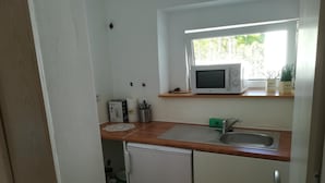 Uma cozinha compacta com micro-ondas, pia e pequena geladeira.