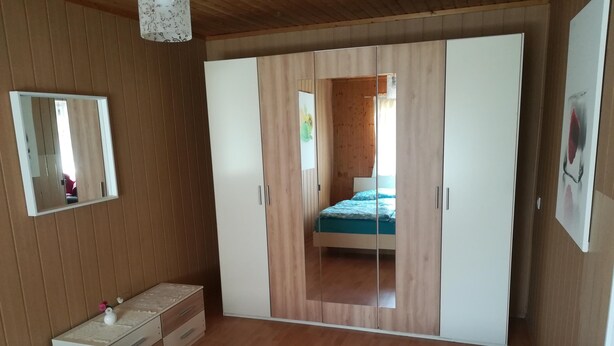 Quarto com guarda-roupa de madeira, mesa de cabeceira e cama com colcha azul.