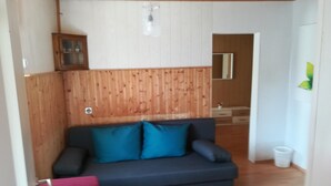 Uma sala de estar com parede de madeira, um sofá escuro com almofadas azuis, um armário de madeira e uma pequena mesa.