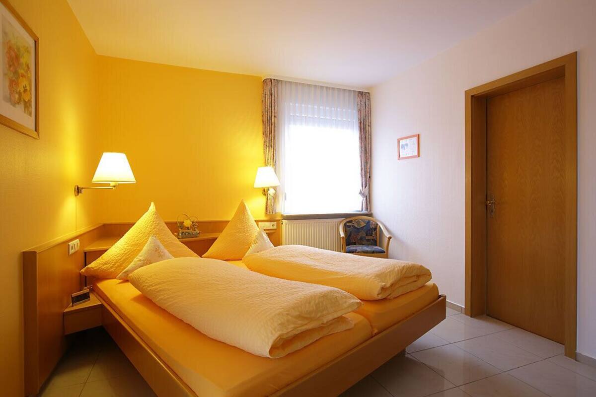 A hotel room with two beds, a window with curtains, a chair, and a door.