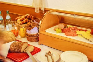 A breakfast buffet with bread, pastries, cheese, meats, and fruits.