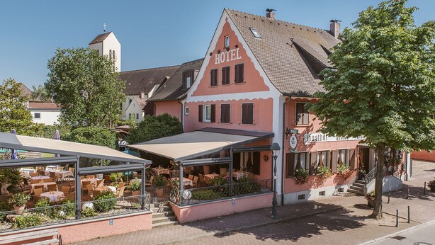 A pink building with a 'HOTEL' sign, a covered outdoor seating area, and a visible entrance. - Hotel-Restaurant Gasthof Adler (Neuenburg am Rhein)