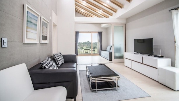 A modern living room with a sofa, a coffee table, a TV, and a balcony with a view. - Oakra Resort (Seogwipo)