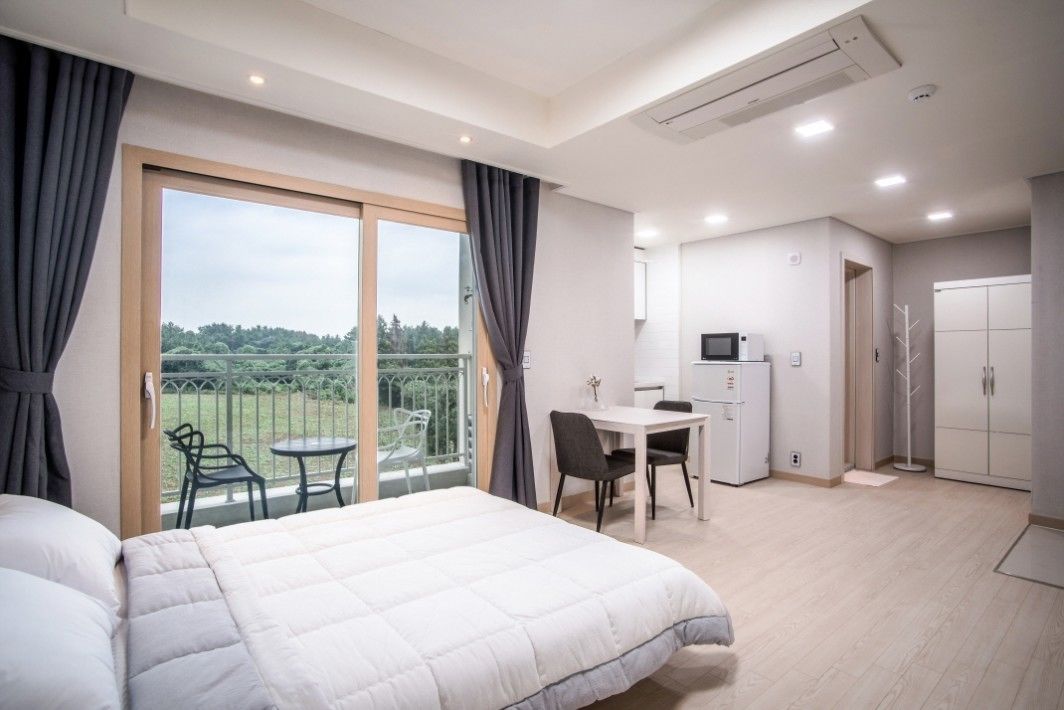 Ein Hotelzimmer mit Bett, Schreibtisch, Stuhl, kleinem Kühlschrank und Blick auf einen Balkon mit Gartenmöbeln.