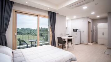 Ein Hotelzimmer mit Bett, Schreibtisch, Stuhl, kleinem Kühlschrank und Blick auf einen Balkon mit Gartenmöbeln.