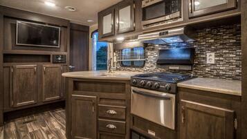 A modern RV kitchen with dark wood cabinets, a stainless steel stove, and a microwave.
