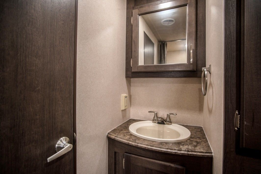 A bathroom with a dark wood door, a white sink, and a mirror above it.