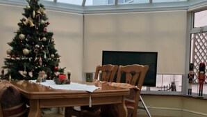 A wooden dining table with chairs, a Christmas tree, and a view of the sky through a large window. - Lovely Family House in Sidcup (Sidcup)