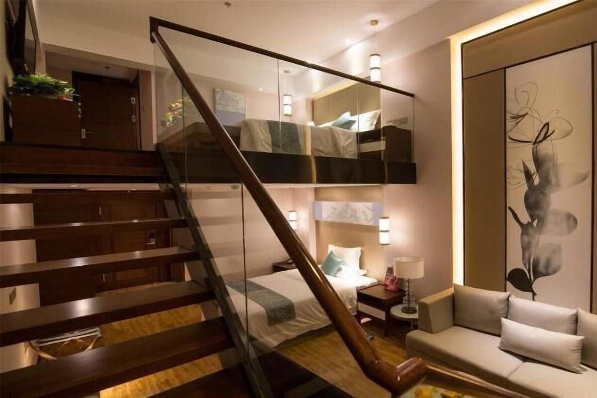 Habitación de hotel moderna con una escalera de cristal, una cama con mesita de noche, un sofá y un cuadro abstracto de gran tamaño.