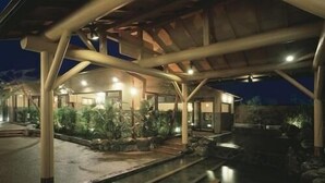Un edificio moderno con un espacio exterior cubierto, senderos de piedra y una fuente de agua.
