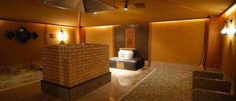 A traditional Japanese onsen with a stone hot spring, a wooden bench, and a tiled floor.