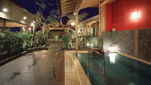 Una piscina interior con cubierta de madera, rodeada de plantas tropicales y un muro de piedra.