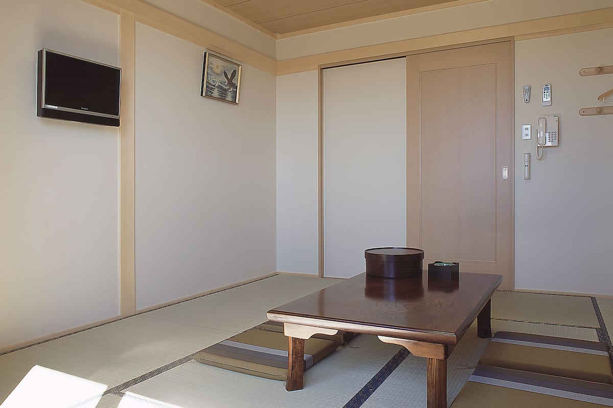 Una habitación japonesa tradicional con suelo de tatami, una mesa de madera baja, un televisor y una puerta corrediza.