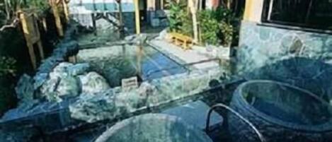 Een wellnessruimte met een jacuzzi, een stenen zwembad en een houten terras.