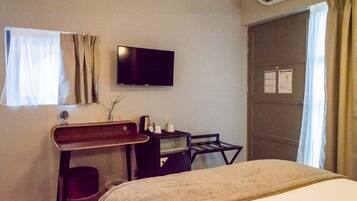 A hotel room with a bed, a desk with a chair, a flat-screen TV, and a window with curtains.