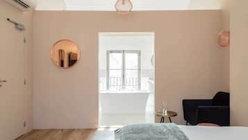 A bedroom with a bed, a round mirror, a small table, a chair, and a balcony view.