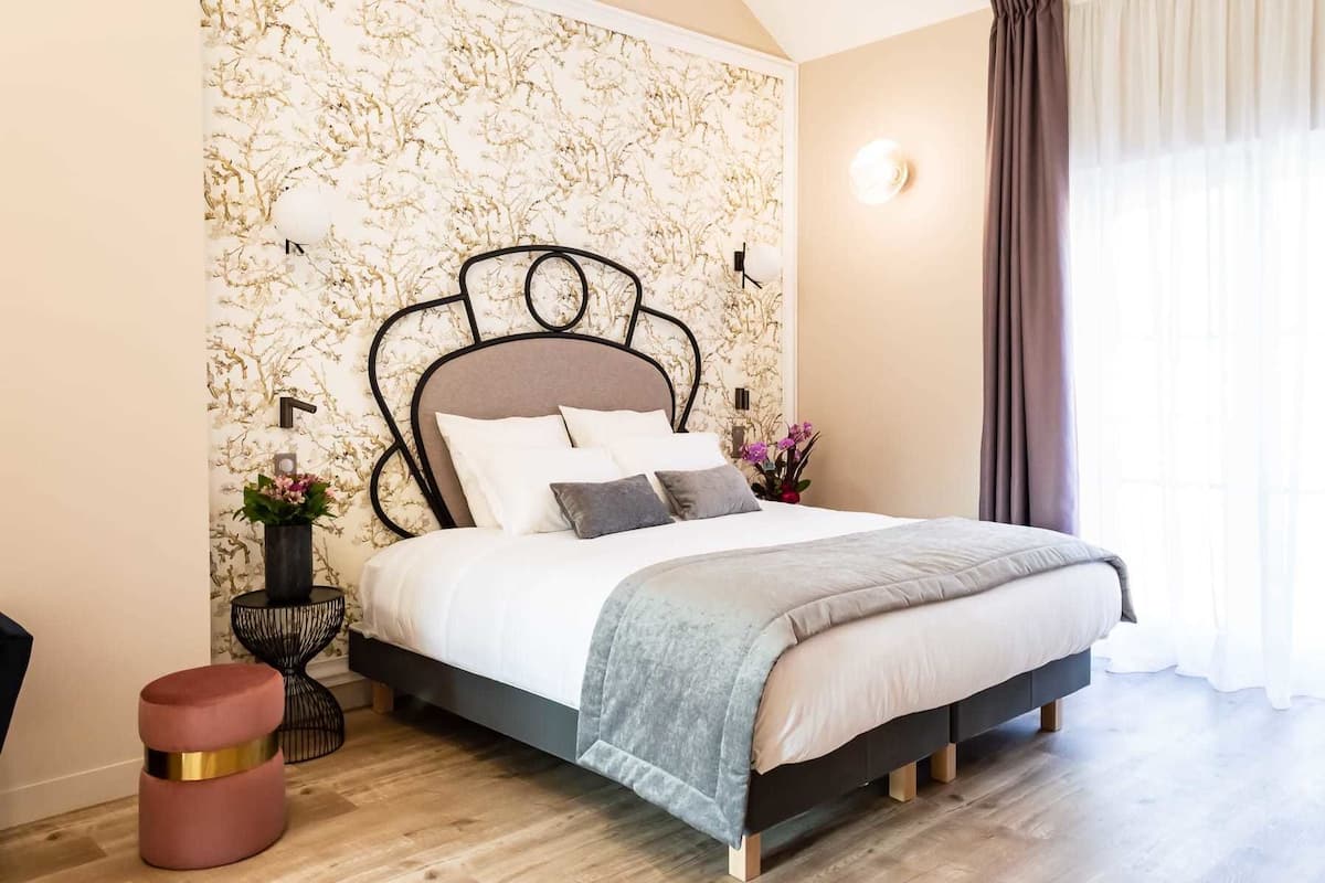 Une chambre moderne avec un grand lit, un mur décoratif et une petite table d’appoint sur laquelle est posé un vase.