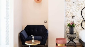 Une pièce moderne avec un fauteuil bleu foncé, une petite table ronde, un pouf rose et une table d’appoint noire agrémentée d’une plante.