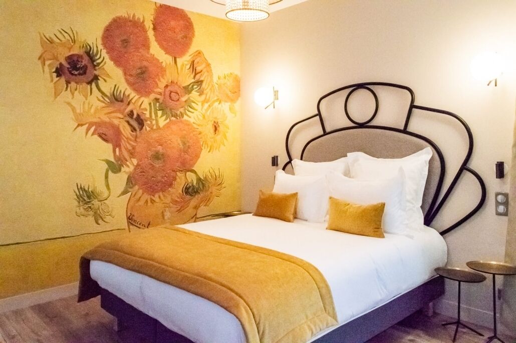 A hotel room with a bed, a wall mural, a bedside table, and a nightstand.