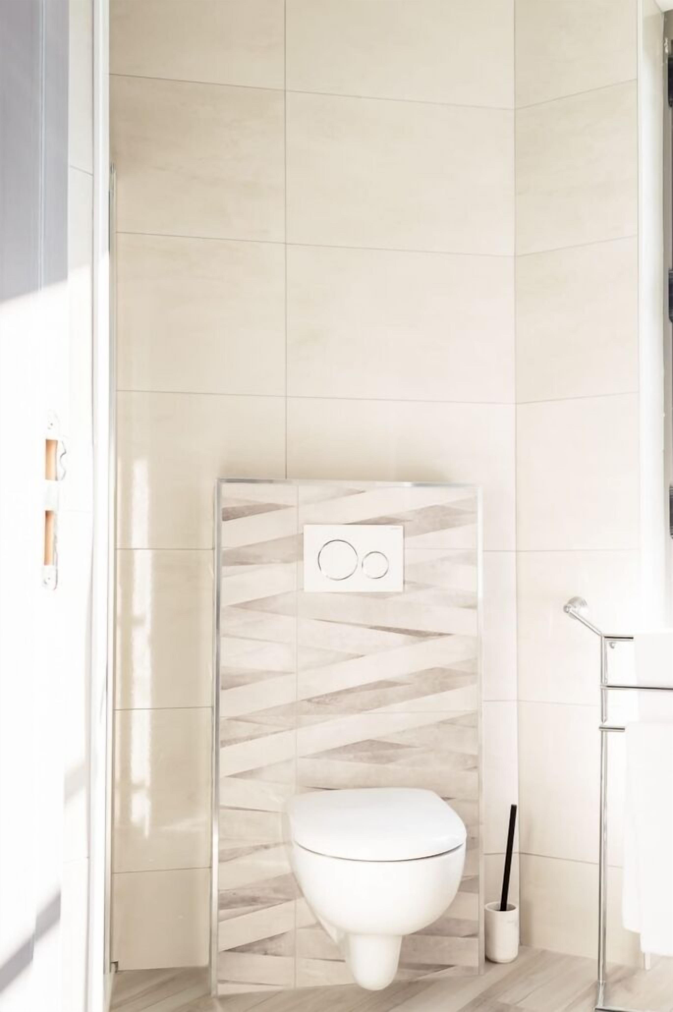 A modern bathroom with a white toilet, a wall-mounted flush handle, and a toilet brush holder.