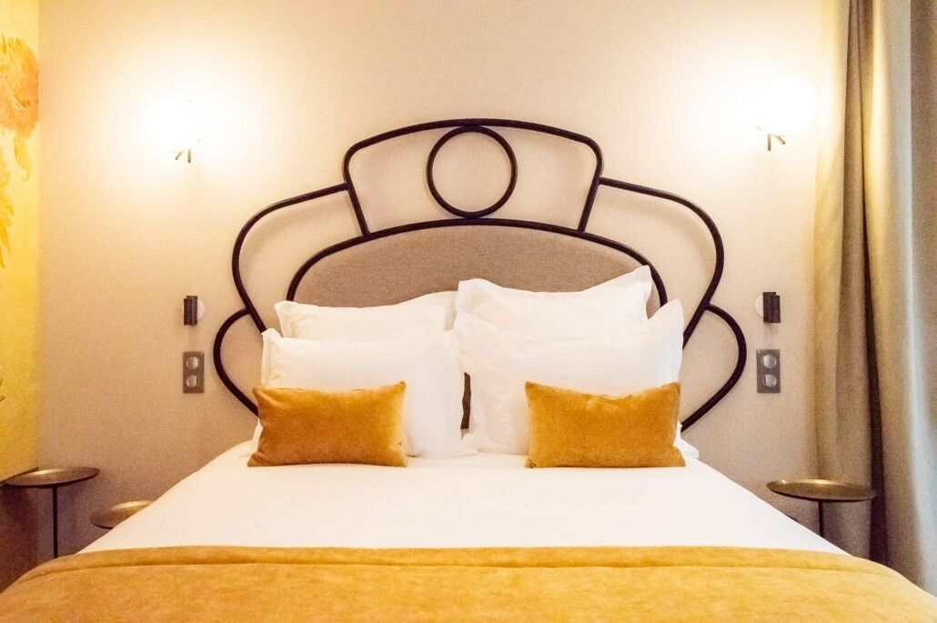 A neatly made bed with white and gold bedding, a metal headboard, and two bedside lamps.
