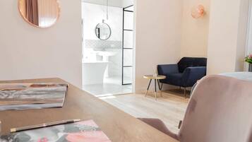 A modern hotel room with a wooden desk, a chair, a round mirror, and a dark blue armchair.