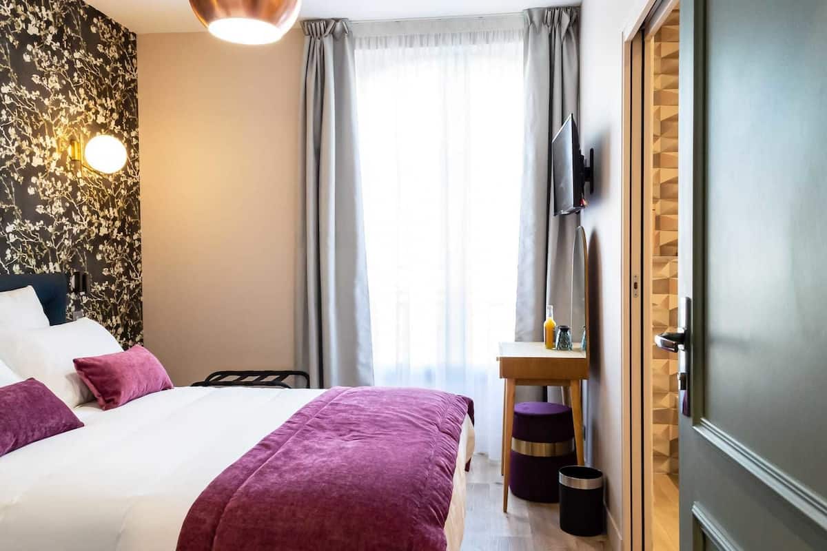 Une chambre d’hôtel équipée d’un lit, d’un bureau, d’une télévision et d’une armoire.