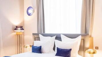 Ett modernt hotellrum med en stor säng, två sängbord, en golvlampa och ett fönster med gardiner.
