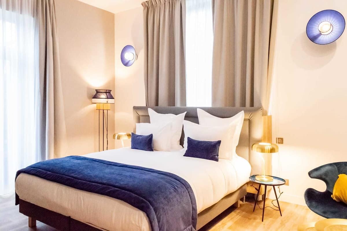 Une chambre d’hôtel moderne avec un grand lit, deux lampes de chevet, une petite table d’appoint et une chaise.