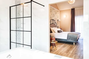 Un dormitorio moderno con una cama grande, una mesita redonda pequeña y un baño con bañera.