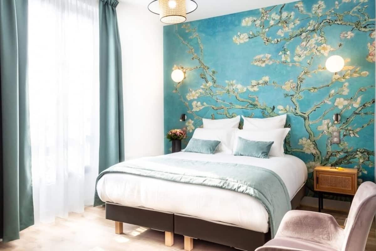 Une chambre à coucher comprenant un lit, une chaise, une table de chevet et un mur recouvert d’un papier peint à motifs floraux.