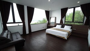 A modern bedroom with a large bed, a leather sofa, and a view of greenery through the windows. - Lakeside Dailai Hotel (Xuan Hoa)