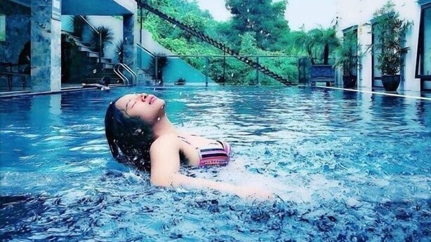 A swimming pool with a person floating, surrounded by buildings and greenery. - Lakeside Dailai Hotel (Xuan Hoa)