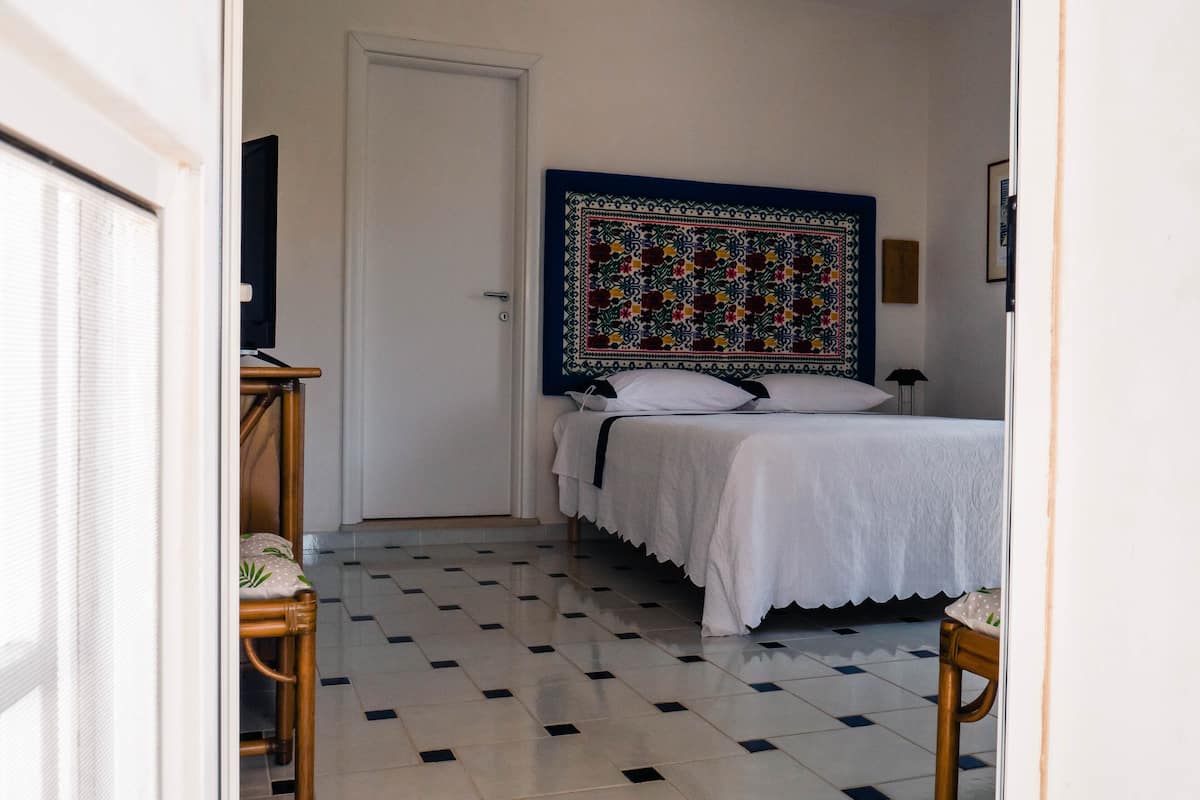 A hotel room with a bed, a chair, a desk, and a large tapestry on the wall.