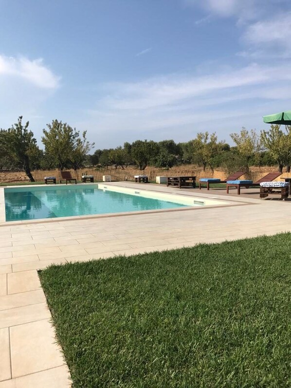 Una piscina con borde de baldosas, rodeada de césped y árboles.