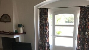A room with a sofa, a television, a coffee table, and a door with curtains. - Casa del Grifone (Carovigno)