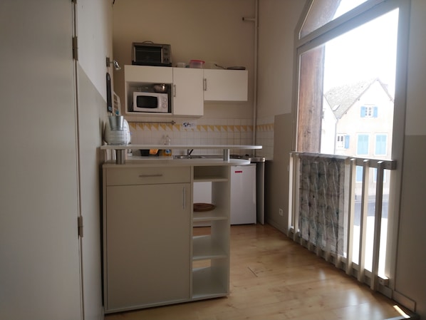 A compact kitchen with a microwave, a small refrigerator, and a sink. There is a window providing a view of the outside.