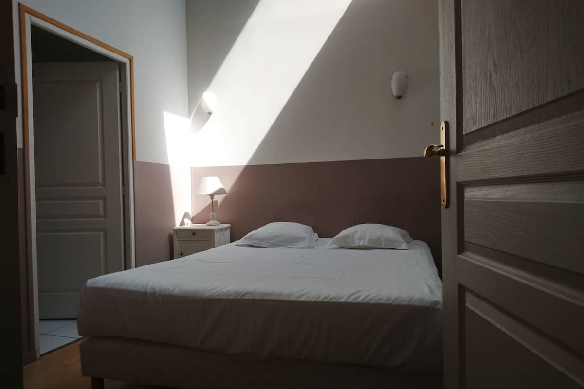 A bedroom with a bed, a nightstand, a lamp, and a door.