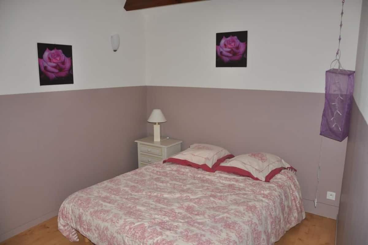 A bedroom with a bed, a nightstand, a lamp, and two wall-mounted pictures of roses.
