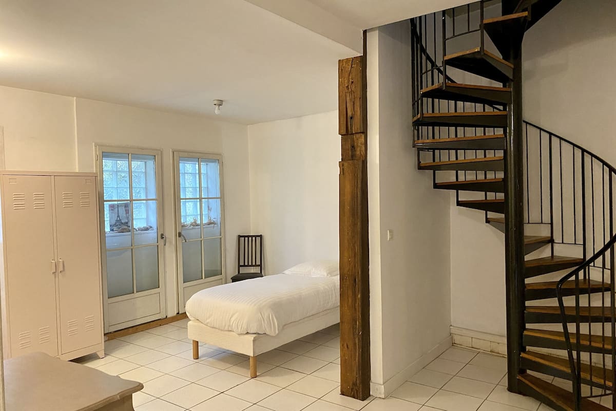 A bedroom with a bed, a desk, a chair, a wardrobe, and a spiral staircase.